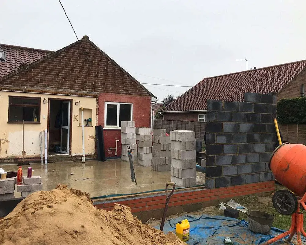 Rear extension under construction on a Norfolk bungalow, with blockwork rising off a new concrete slab and a cement mixer on site
