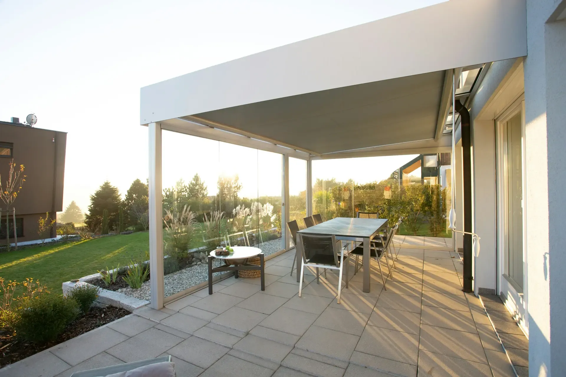 Large paved patio in slab-laid stone running from the rear of a house out to a lawn, with a covered dining area alongside